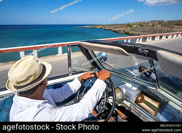 Taxi driver driving a vintage convertible car at the coast on Cuba