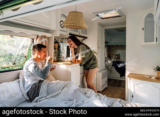Happy woman leaning on table by boyfriend drinking coffee in camper
