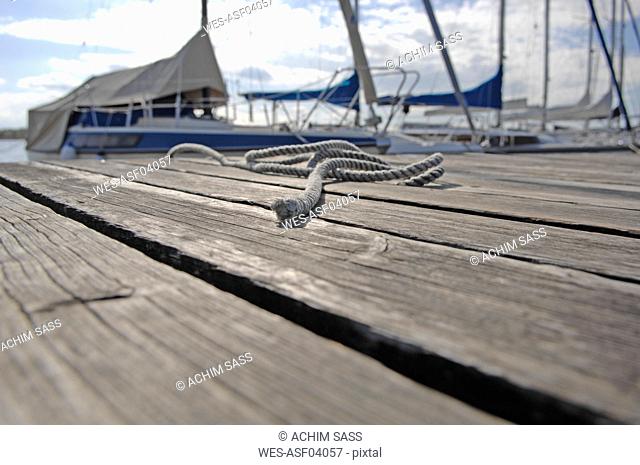 Germany, Bavaria, Lake Ammersee, Rope on jetty with sailing ships in background