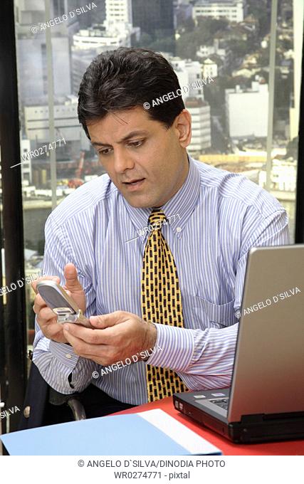 Executive looking at screen of mobile with worried expression in office at top floors of skyscraper in modern city MR 687U