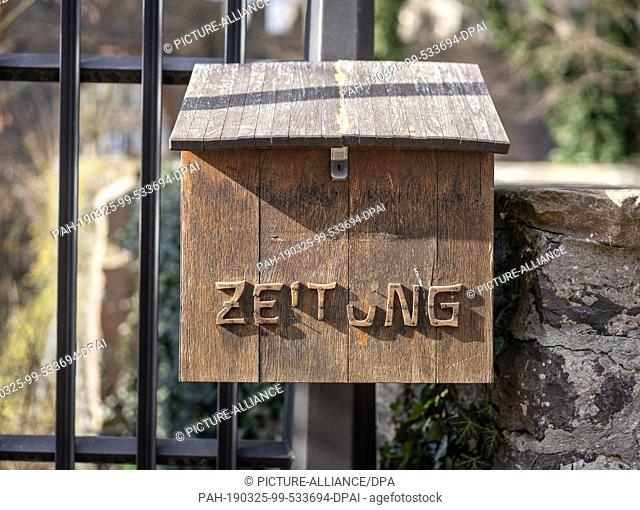 09 March 2019, Hessen, Echzell: A wooden box for the delivery of newspapers with partially fallen letters hangs on a fence
