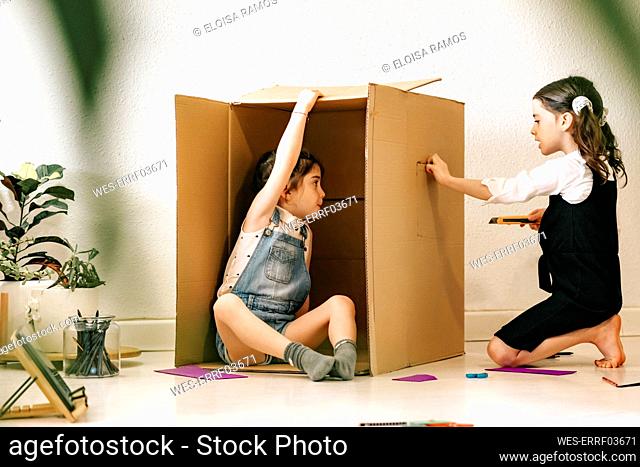 Two little sisters building house with cardboard box