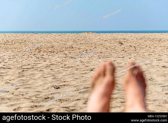 Sandy beach with the sea on the horizon, in the foreground blurred feet of tourist lying in the sand