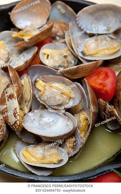 fresh clams stewed on an iron skillet over wite rustic wood table