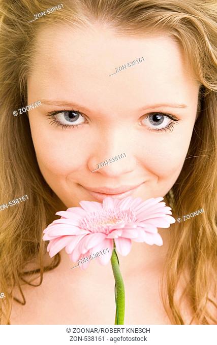 Blondes Mädchen hält lächelnd eine rosa Gerbera