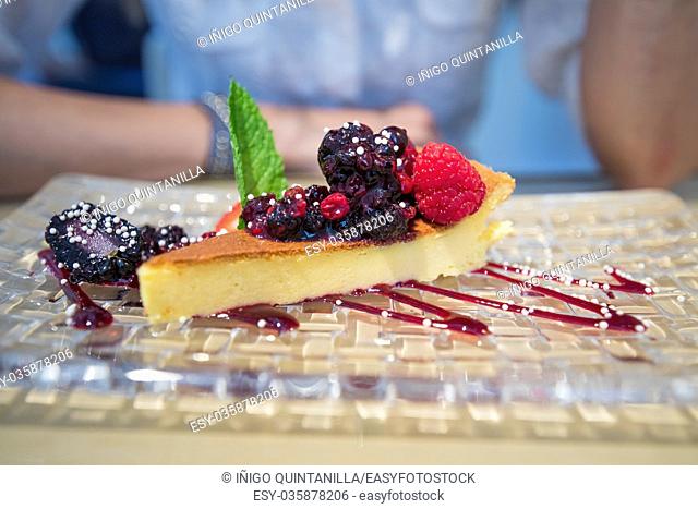 portion of cheese cake with strawberry jam with red fruits berries and green mint leaf in glass tray next to woman