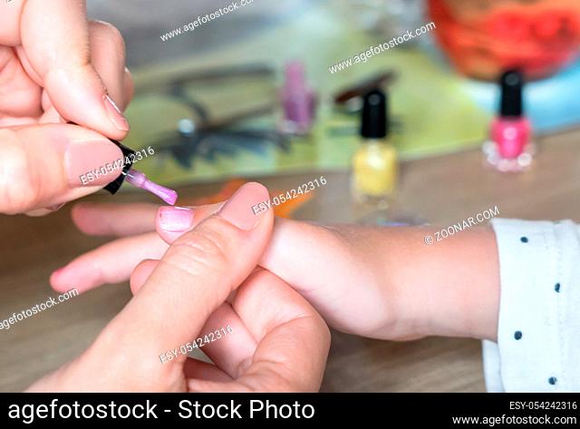 Hands of a woman who puts a violet nail polish on the nails of a little girl. Defocused background