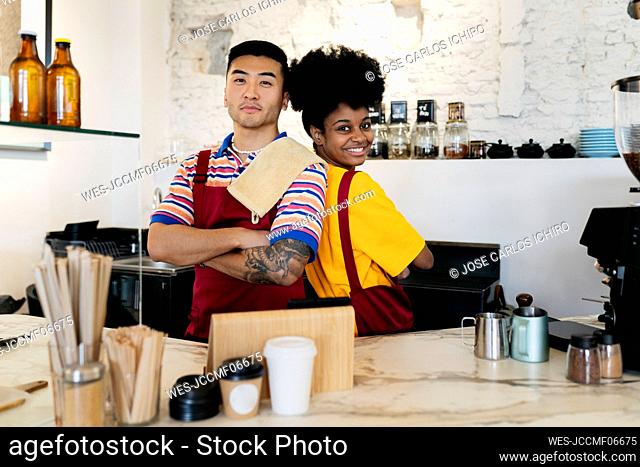 Smiling woman standing with arms crossed by colleague at checkout