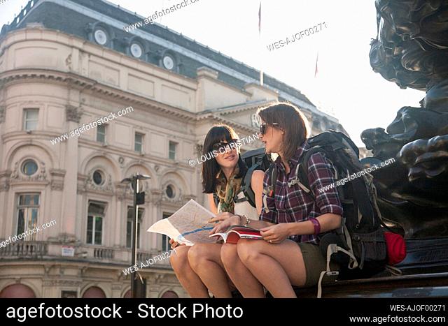 Female backpackers discussing over map while sitting at town square