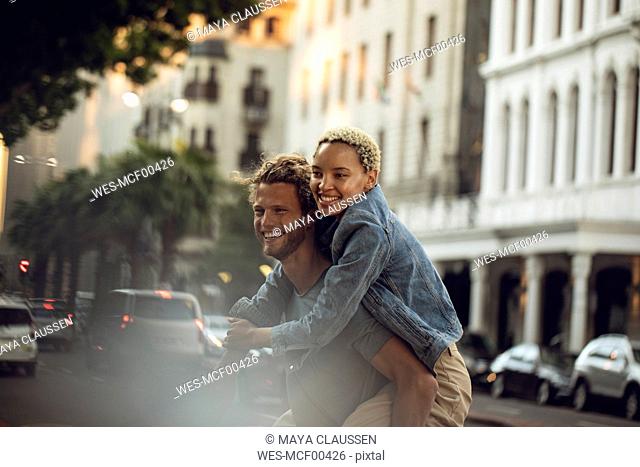 Happy young man carrying girlfriend piggyback in the city