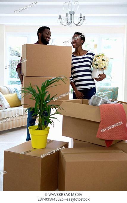 Couple carrying big cardboard box and vase at new home