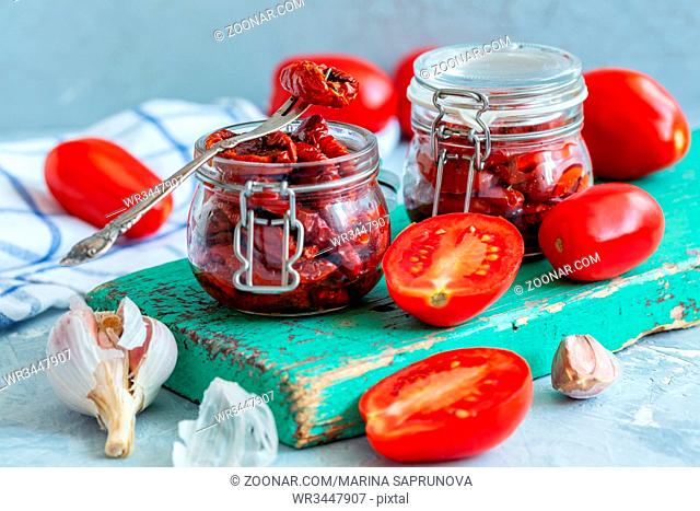 Glass jars with homemade spicy sun-dried tomatoes on an old wooden board