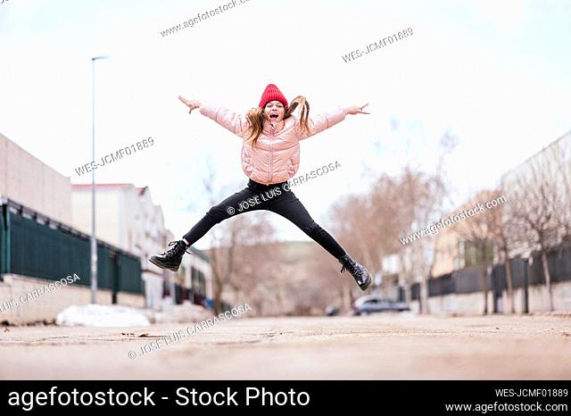Cheerful girl jumping on road against sky