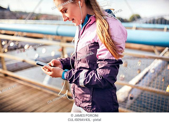 Mid adult female runner choosing smartphone music on footbridge