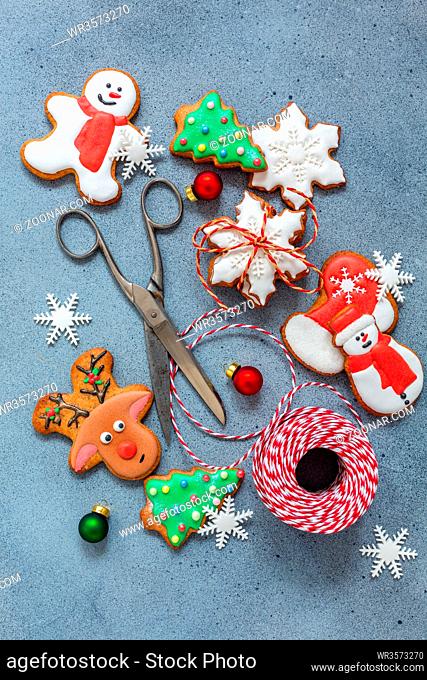 Christmas gingerbread with icing sugar, snowflakes, scissors and a colored cord on a gray textured background. Gift idea. Top view