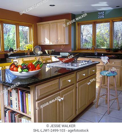 KITCHEN - Island, medium wood cabinets, paneled doors, range in island, cookbooks, dark green granite countertops, bowl of vegetables, tile floor
