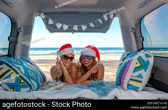 Two traveling girls celebrate Christmas by the beach in Australia. They are leaning into their van with fingers in V good vibes