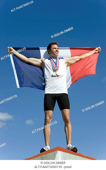 Male athlete being honored on podium, holding up French flag