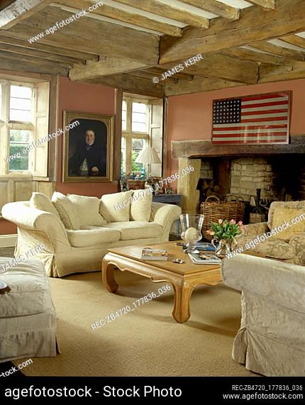 Rustic, country sitting room with wood beamed ceiling, framed American flag, and a comfortable seating area in front of an inglenook fireplace