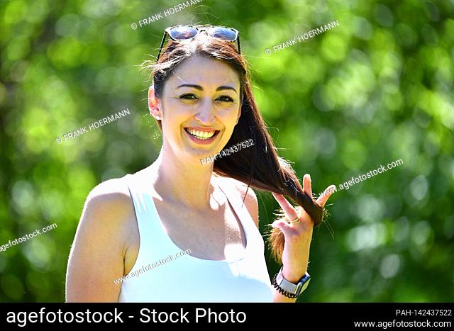 Pretty long-haired young woman (30 years old) in a white top looks smiling at the camera. Model released! | usage worldwide