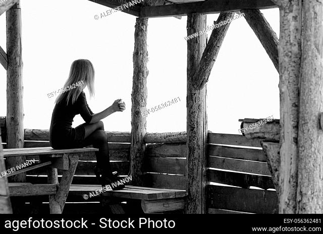 A girl sits in a wooden arbor on a foggy day and looks into the distance