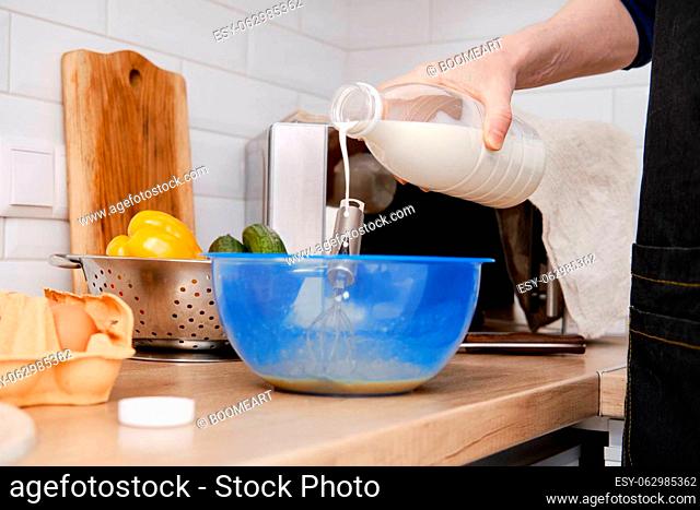 Closeup view of hands of a man pouring milk in a bowl with beaten eggs to make an omelet