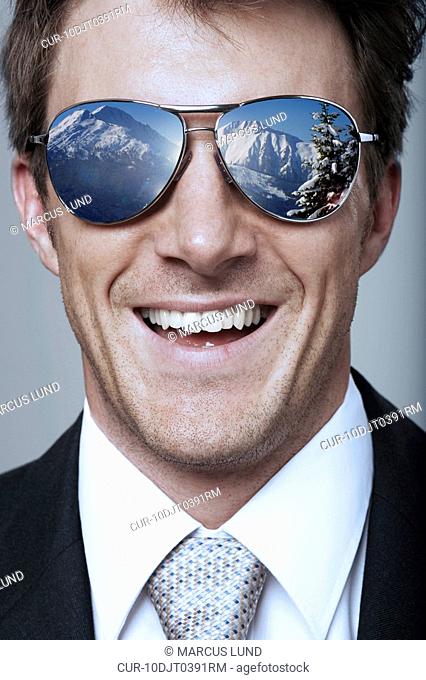 Smiling business man wearing sunglasses with reflection of snowy mountains