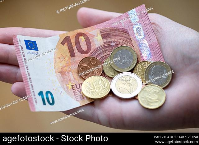 ILLUSTRATION - 09 April 2021, Bavaria, Nuremberg: A woman holds notes and coins in her hand. The savings rate in Germany was at a record high of 16