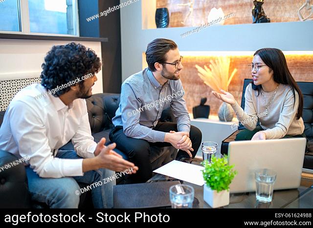 Smiling female supervisor conversing with her company workers seated around the table in her office