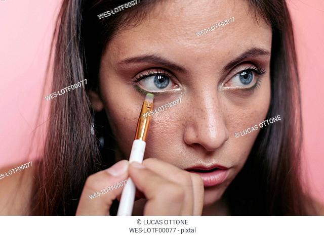 Close up of a young brunette woman with beautiful blue eyes applying eyeshadow with an eye brush