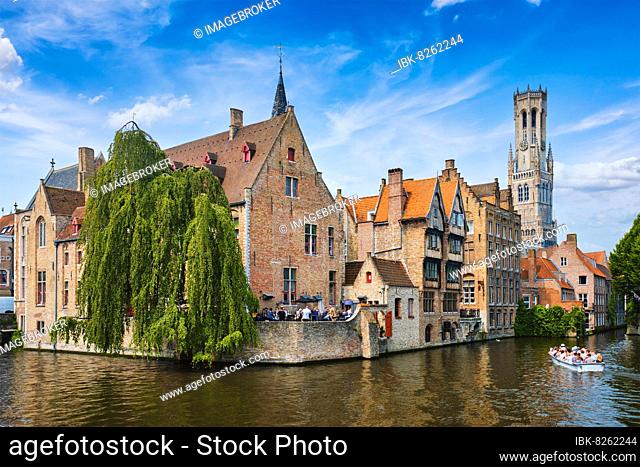 Famous view of Bruges tourist landmark attraction, Rozenhoedkaai canal with Belfry and old houses along canal with tree and tourist boat, Brugge, Belgium