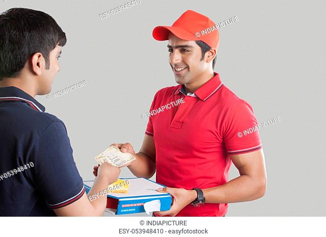 Young delivery man delivering pizza to customer over gray background
