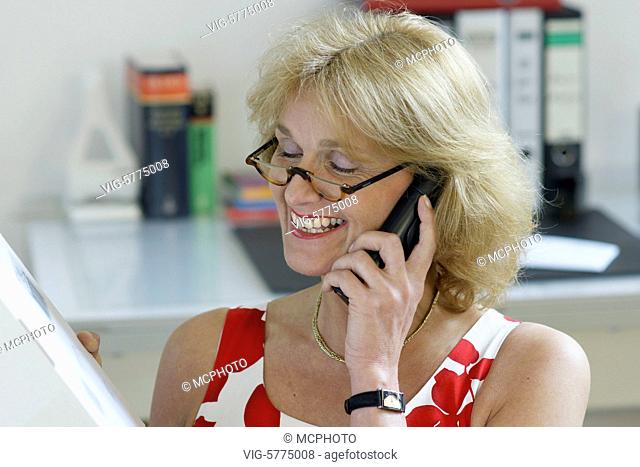 Eine Frau sitzt vor dem Computer-Monitor, hat ein Paket in der Hand und telefoniert, MR, 2008 - Hamburg, Hamburg, Germany, 13/02/2008