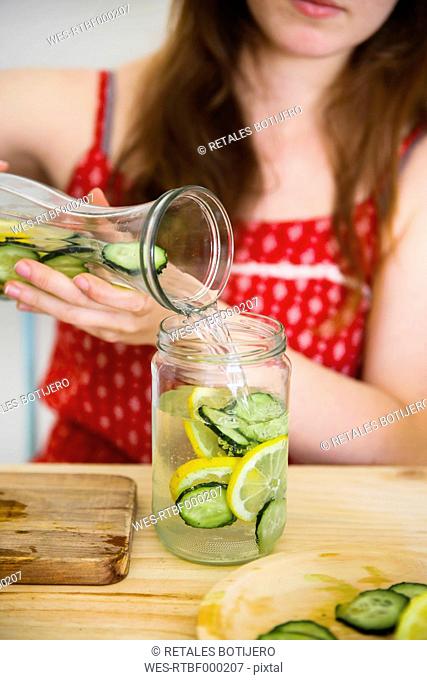 Woman pouring detox water infused with lemon and cucumber into a glass