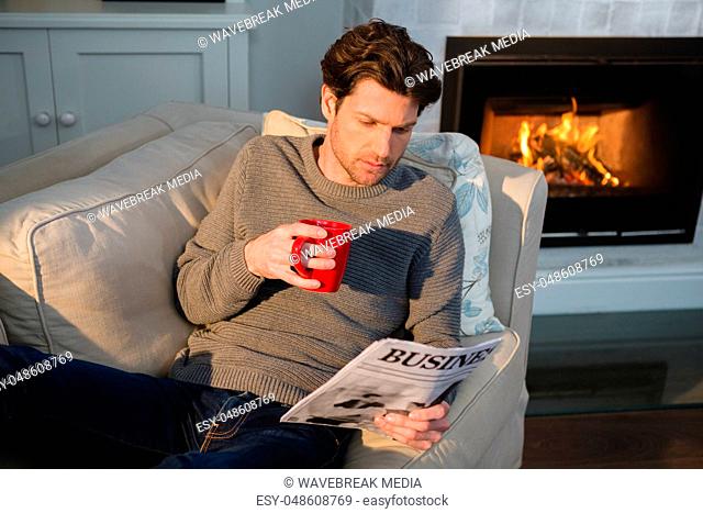 Man reading newspaper while having coffee in living room