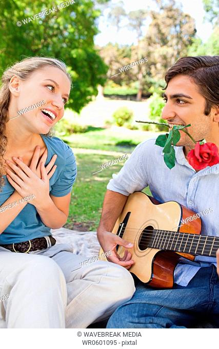 Man with a rose in his mouth playing a song for his girlfriend