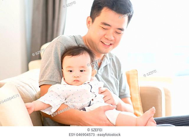 Father holding baby sitting on sofa