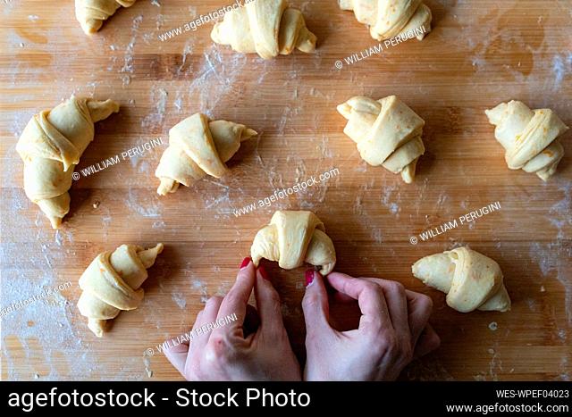 Woman rolling up croissants on cutting board in kitchen