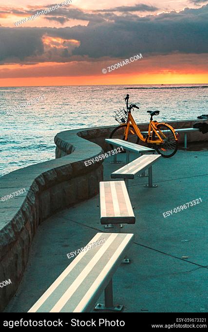 A yellow bicycle and empty bench seats overlooking the ocean at sunrise