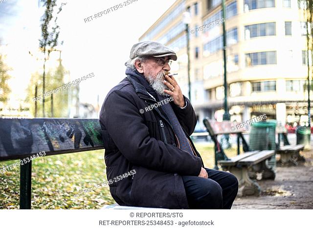Belgium , Brussels , Nov 24 , 2017 - Homme retraité assis sur un banc - Solitaire -Fumant une cigarette - Lisant le journal - Homme devant un lac - Seul dans un...