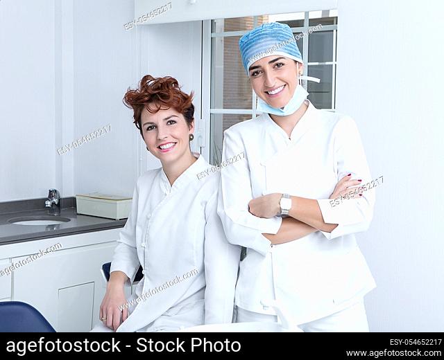 Happy adult women in medical uniform smiling and looking at camera while working in modern office in dental clinic