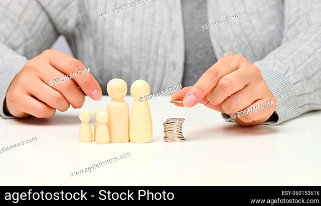 female hand puts coins in a pile and wooden figurines of a family on a white table. Economy and investment concept, budget planning