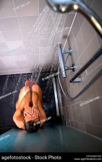 Pretty, young woman taking a long hot shower washing her hair in a modern design bathroom