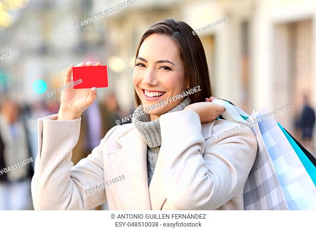 Portrait of a happy customer showing a blank credit card on the street in winter