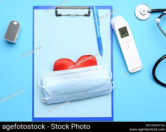 mask and pulse oximeter, electronic thermometer and other medical supplies on a blue background, top view