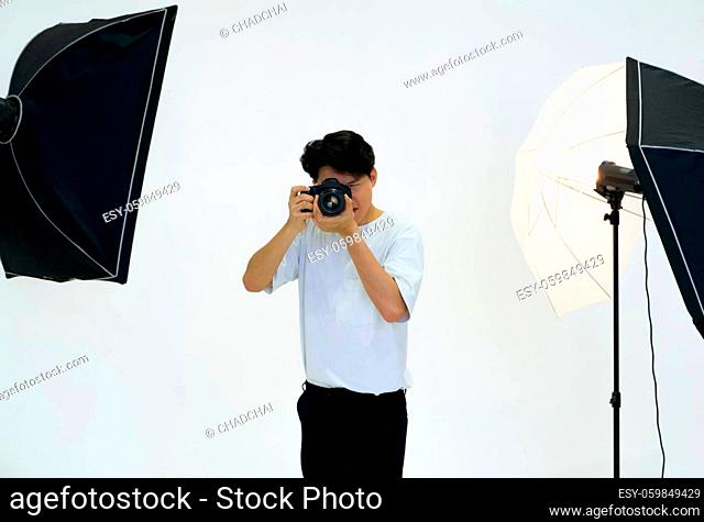 Young asian photographer looks through the viewfinder while shooting with the camera. Working atmosphere in the photo studio