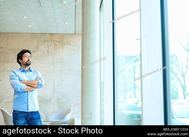 Thoughtful businessman with arms crossed standing in office