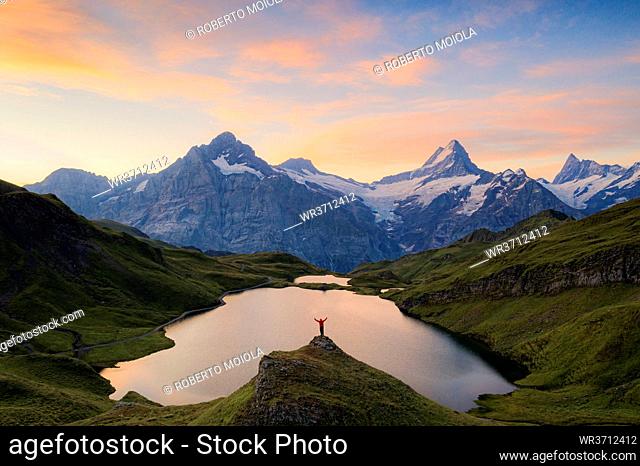 Cheerful hiker admiring Wetterhorn, Schreckhorn and Finsteraarhorn from Bachalpsee at dawn, Bernese Oberland, Switzerland, Europe