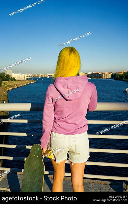Young woman looking at sea while standing on bridge during sunny day