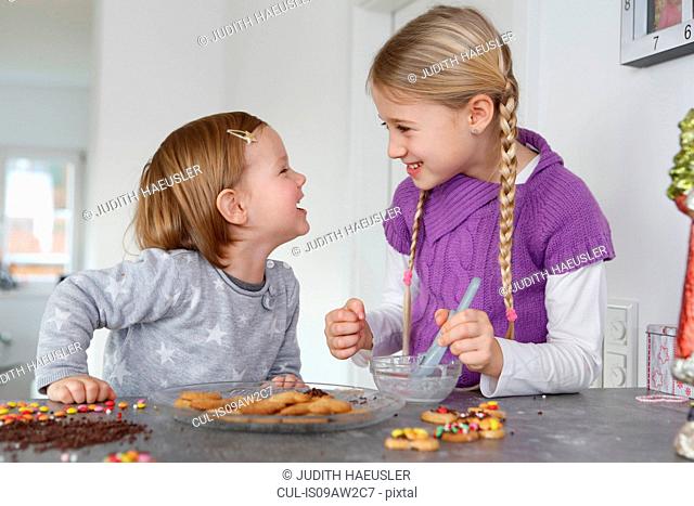 Girls at kitchen counter decorating cookies face to face smiling